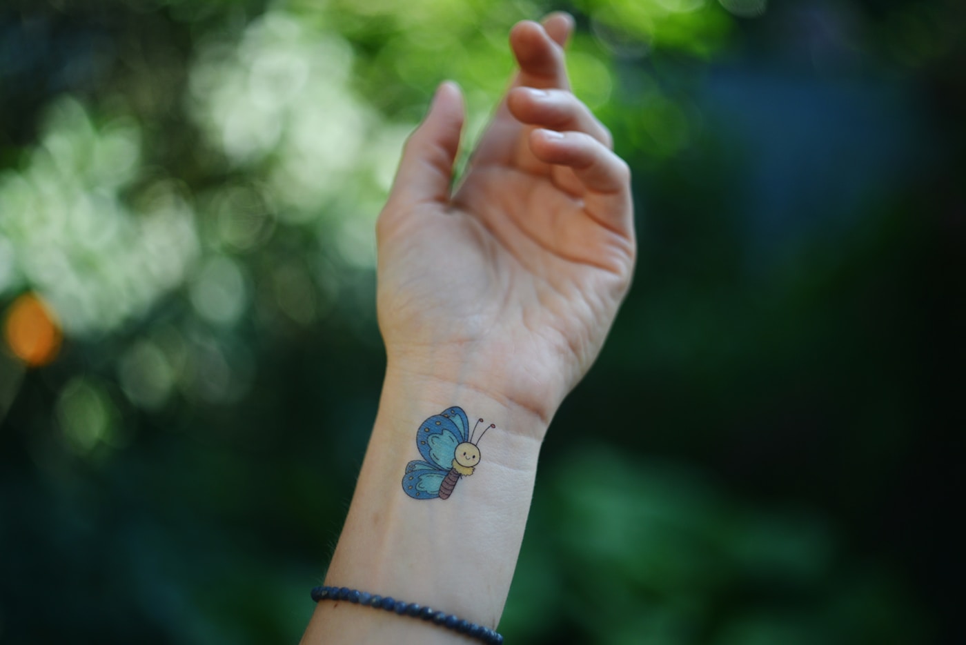Detaljerad fine line-tatuering av en fjäril med halvmåne på insidan av en handled, tunna linjer och subtila skuggor
