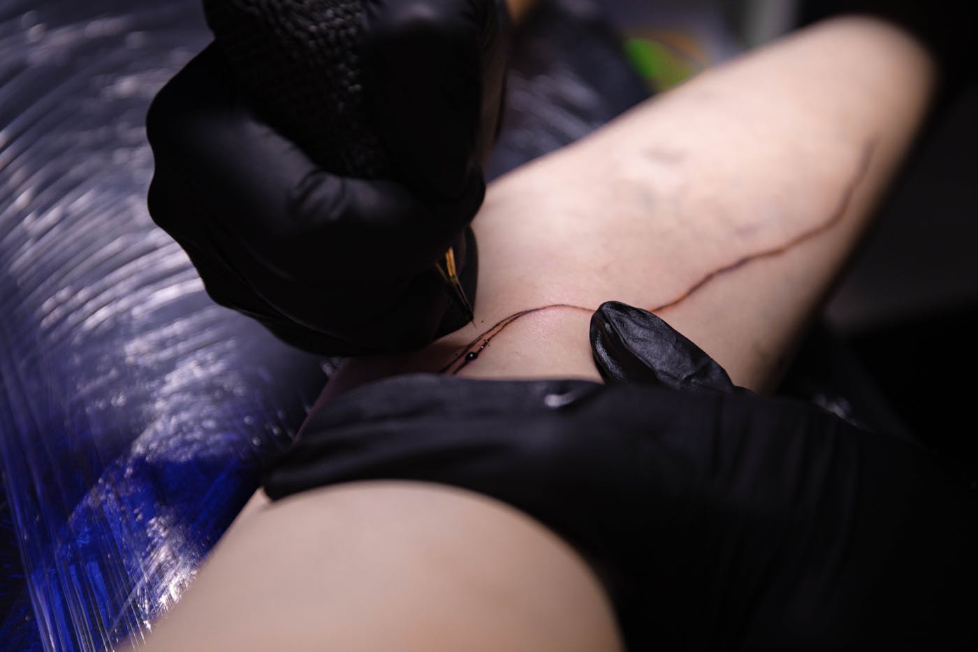 Sam Rivera koncentrerad vid arbetsbordet, en geometrisk skiss under arbete, tatueringsmaskin och bläck i förgrunden